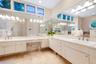L-shaped vanity featuring a solid surface countertop, dual integrated sinks with brushed metal faucets, extensive built-in cabinetry, large-scale wall