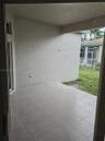 Covered concrete patio featuring large-format ceramic floor tiles, textured stucco walls, and an open entryway to the exterior grounds