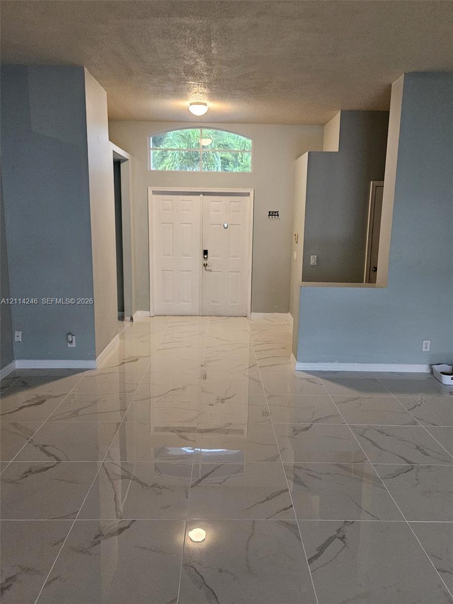 Entryway featuring large-format tile flooring with a neutral veined pattern, double front doors, and a semi-circular transom window