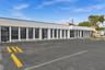 Commercial exterior featuring a flat roofline, floor-to-ceiling glass windows, a white facade, and an asphalt parking lot with designated wheel stops