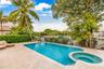 Outdoor pool featuring a built-in spa, paved stone patio, black metal fencing, and mature landscaping