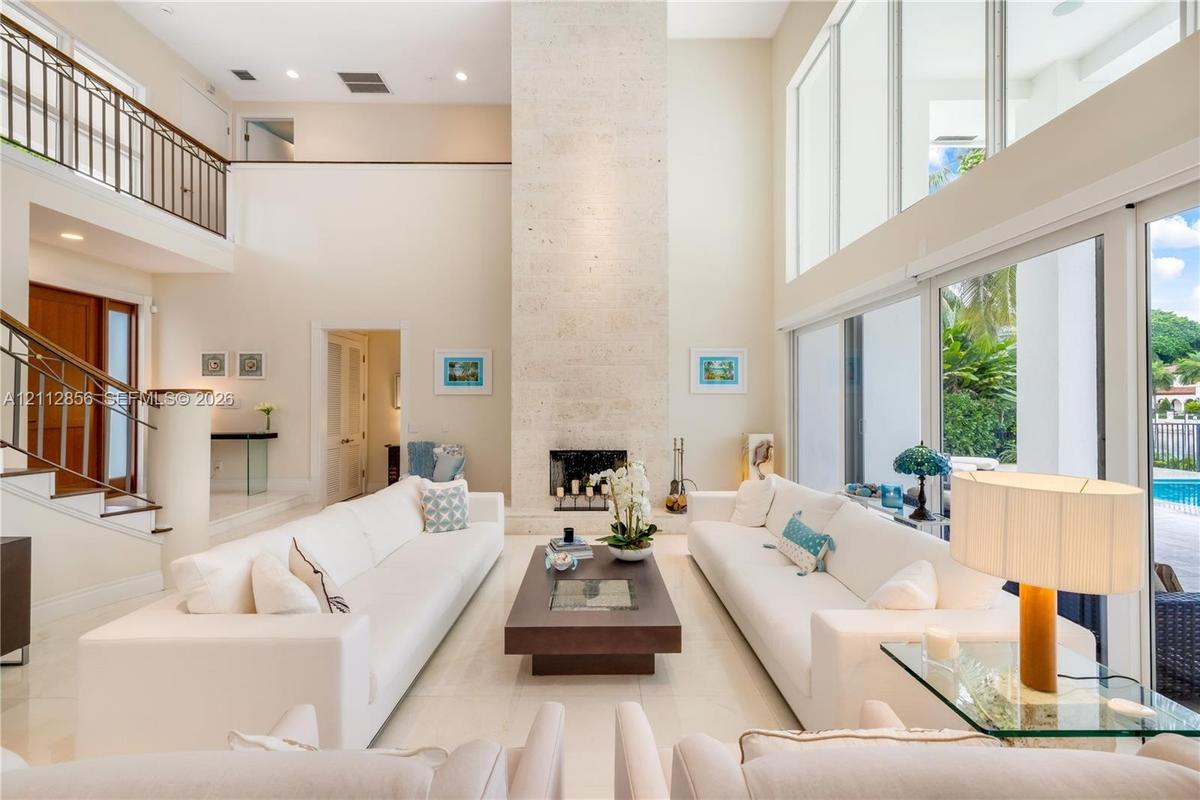 Double-height living area featuring a floor-to-ceiling stone fireplace, expansive glass wall panels, a mezzanine balcony with metal railing, and polis