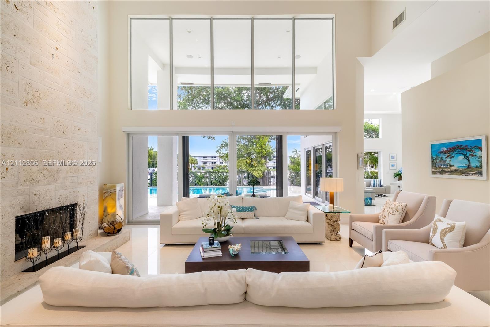 Double-height living area featuring floor-to-ceiling windows, a full-height stone-clad fireplace, polished tile flooring, and sliding glass doors