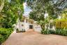 Stucco exterior featuring a circular accent window, elevated entryway with stone steps, multi-car garage, and a spacious paved driveway shaded by matu