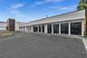 Commercial building exterior featuring a white smooth-finish facade, extensive floor-to-ceiling glass paneling, and an asphalt parking area with marke