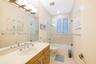 Bathroom featuring wood-finish cabinetry, an integrated sink with a chrome dual-handle faucet, a full-width vanity mirror, and a tub-shower combinatio
