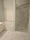 Walk-in shower with stone-finish tile surround, ceiling-mounted rainfall shower head, glass enclosure, built-in soaking tub, and large-format tile flo