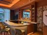 Custom bar featuring a stone countertop, built-in wooden cabinetry, recessed tray ceiling lighting, and decorative wall paneling