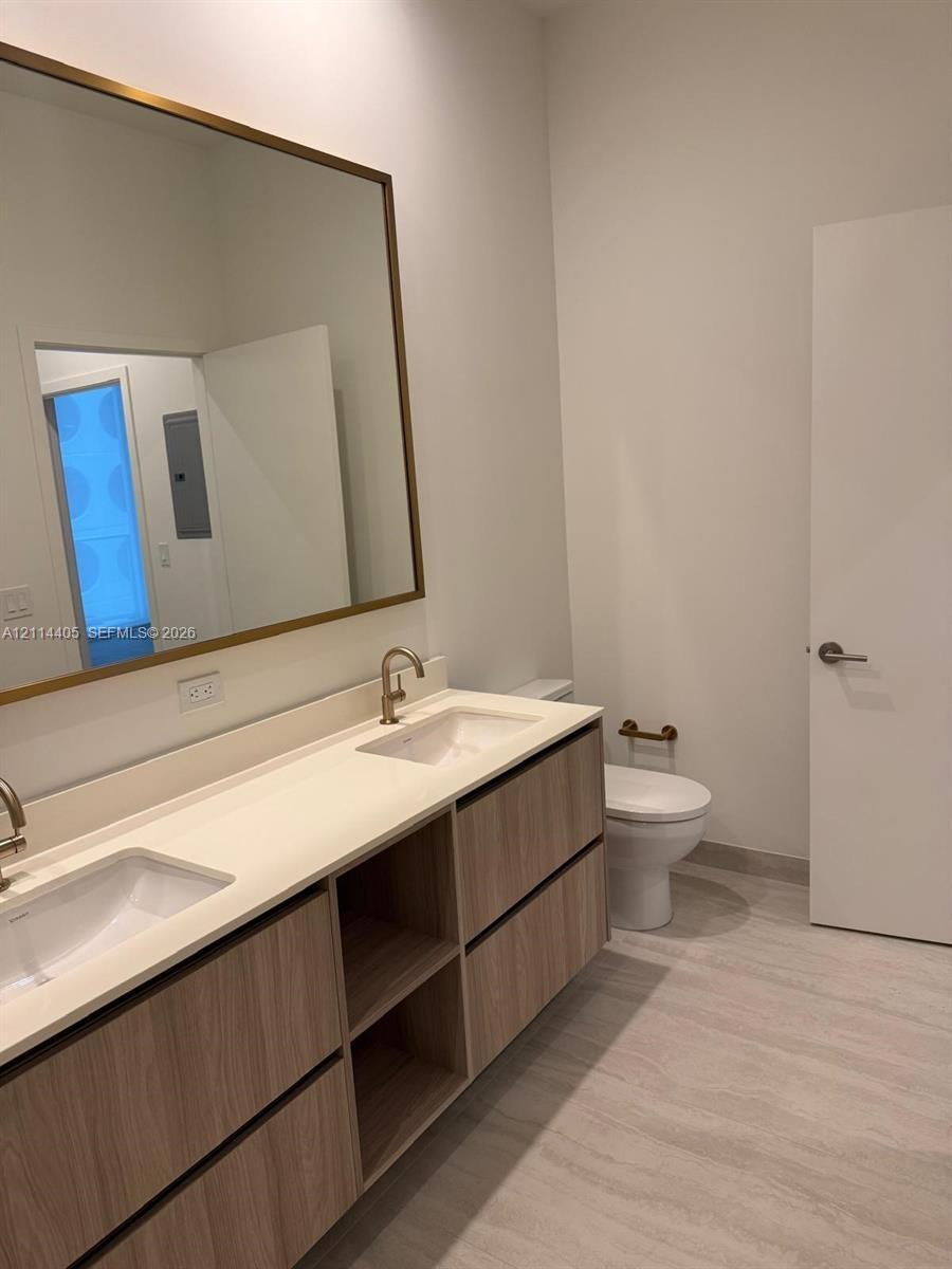 Floating wood-finish vanity with a double-basin countertop, undermount sinks, brass-toned fixtures, and a large rectangular mirror with a matching fra