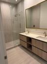 Floating dual-vanity with wood-finish cabinetry, white countertop, integrated rectangular sinks, brass-toned fixtures, and a glass-enclosed shower wit