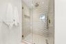 Walk-in shower featuring a chevron-patterned tile accent wall, glass enclosure, recessed wall niche, rainfall showerhead, and a handheld fixture