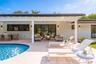 Covered outdoor patio featuring board-and-batten siding, recessed lighting, multi-panel sliding glass doors, and a stone-paver pool deck surrounding a
