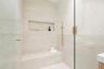Walk-in shower featuring herringbone-patterned tile wall accents, built-in bench seating, recessed wall niche, and gold-finish hardware behind a glass