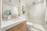 Bathroom featuring a wood-finish vanity with a quartz countertop, brass-toned fixtures, a walk-in shower with chevron-patterned tile, and two floating