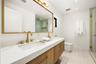 In suite Bathroom Double vanity featuring wood-finish cabinetry, white countertop with dual undermount sinks, gold-tone fixtures, and a large wood-fra