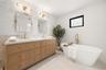 Double vanity with wood-finish cabinetry, quartz countertops, herringbone-patterned tile backsplash, polished brass fixtures, and a freestanding soaki