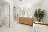 Double vanity with wood-finish cabinetry, countertop with integrated dual sinks, gold-tone wall-mounted lighting, glass-enclosed shower with tile surr