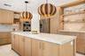 Kitchen featuring light wood-finish cabinetry, a waterfall-edge stone countertop island, built-in stainless steel appliances, decorative textured pend