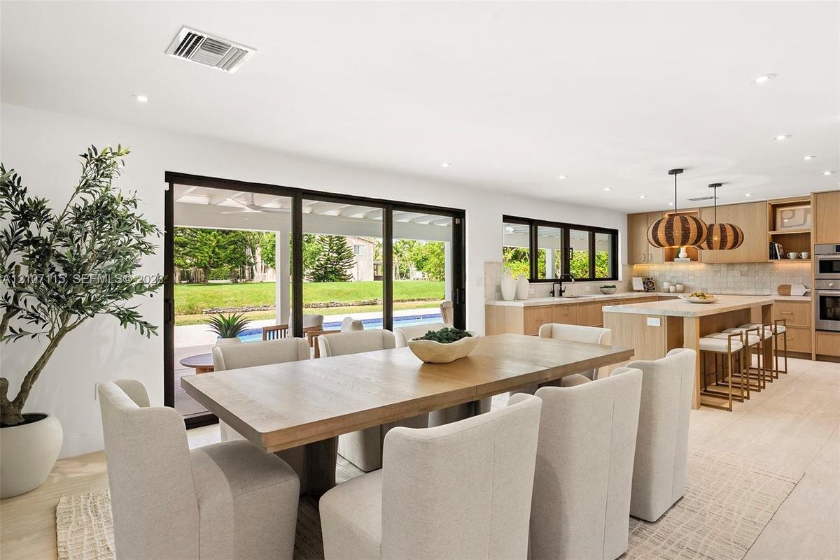 Open-concept kitchen and dining area featuring light wood-finish cabinetry, a large kitchen island with integrated seating, recessed lighting, and exp