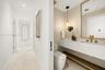 Powder room Floating vanity with stone-surfaced countertop, integrated rectangular sink, brass-finish fixtures, textured wall covering, and pendant li
