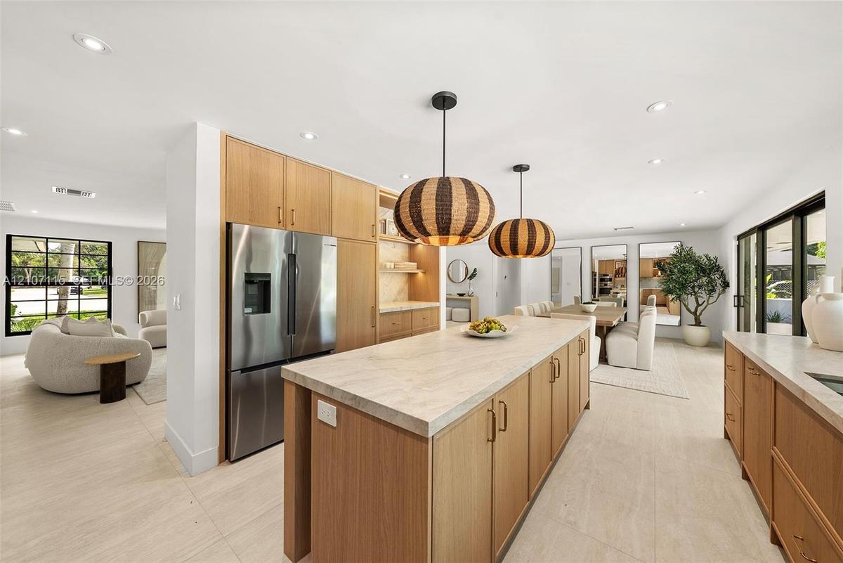 Kitchen featuring wood-finish cabinetry, a large central island with light-toned countertop, stainless steel refrigerator, recessed lighting, and larg