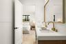 Dual-sink vanity with quartz countertop, brass-toned fixtures, wood-finish cabinetry, and a large framed mirror