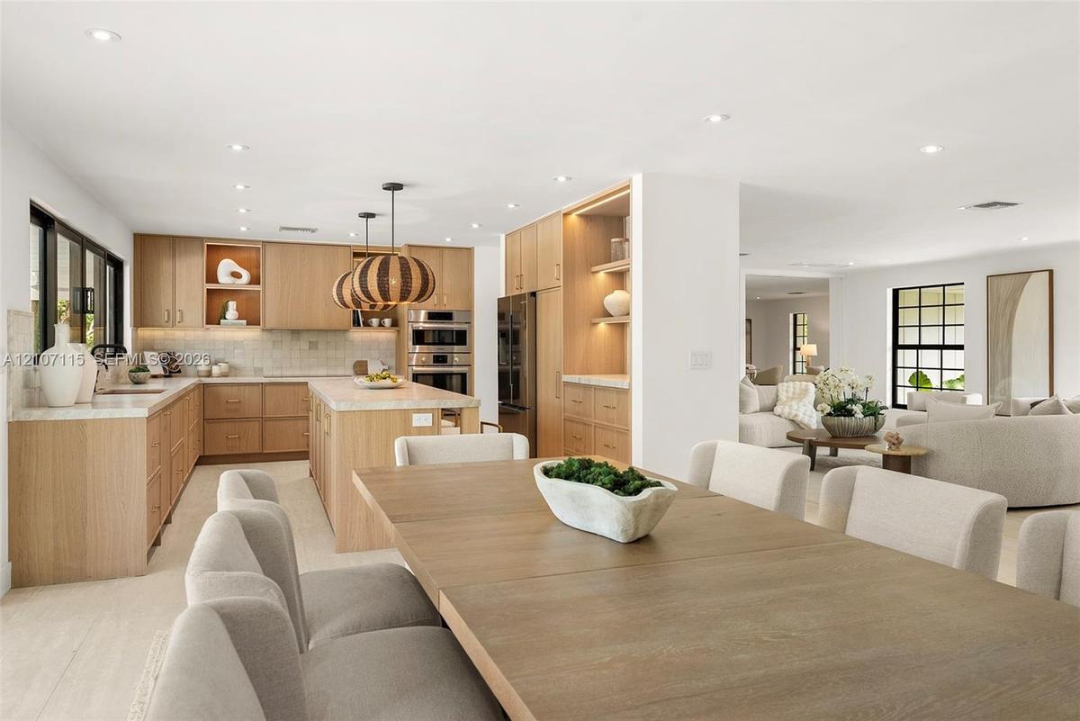 Custom wood cabinetry with integrated lighting, stone countertops, stainless steel built-in double ovens, recessed lighting, and large-format tile flo