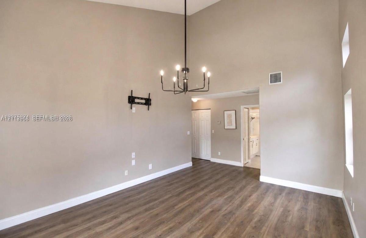 High-vaulted ceilings, dark wood-finish flooring, and a prominent six-light chandelier featuring a matte black finish