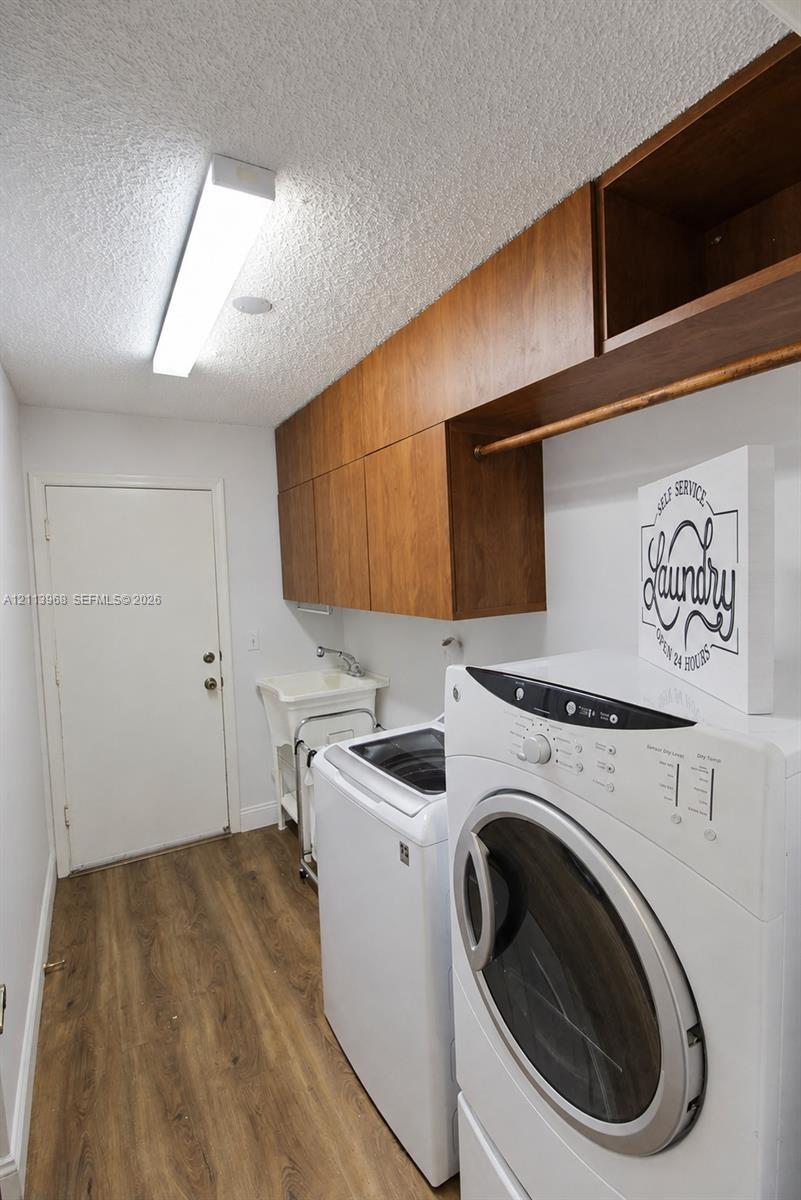 Laundry area featuring wood-finish cabinetry with an integrated hanging rod, wood-finish flooring, a utility sink, and a linear overhead light fixture