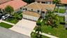 Two-story residence featuring a tile roof, three-car garage, concrete driveway, and landscaped yard with palm trees
