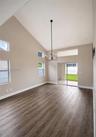 Vaulted ceilings, wood-finish flooring, multi-level windows, modern chandelier, and sliding glass doors