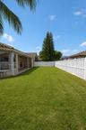 Expansive backyard featuring a level lawn, covered patio, and perimeter white vinyl privacy fencing
