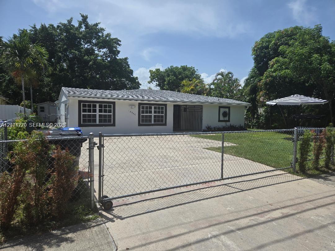 Single-story exterior featuring white stucco siding, a concrete driveway, a sliding chain-link entry gate, and a hip roof