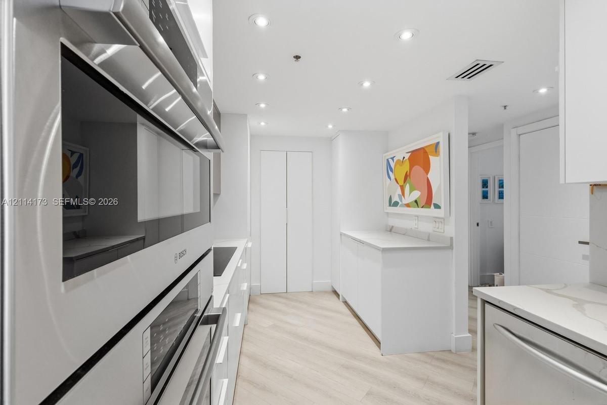 Kitchen featuring integrated wall ovens, white cabinetry, solid surface countertops, recessed lighting, and wood-finish flooring