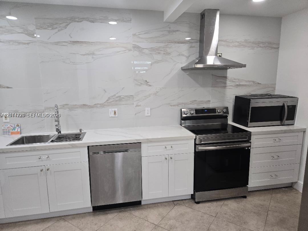 Kitchen featuring white cabinetry, large-format stone-patterned tile backsplash, stainless steel appliances, and solid surface countertops