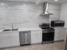 Kitchen featuring white cabinetry, large-format stone-patterned tile backsplash, stainless steel appliances, and solid surface countertops