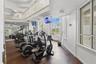 Two-story fitness space featuring wood-finish flooring, floor-to-ceiling windows, an elevated mezzanine railing, and expansive mirrors