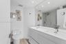Dual-vanity cabinet with integrated rectangular sinks, expansive wall-to-wall mirror, glass-enclosed shower, and wood-finish flooring