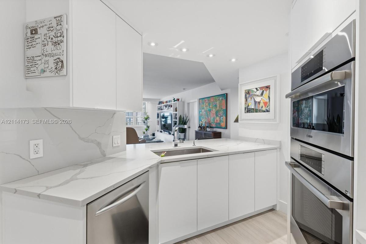 Kitchen featuring white cabinetry, veined solid-surface countertops, stainless steel undermount sink, and integrated stainless steel double wall ovens