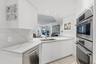 Kitchen featuring white cabinetry, veined solid-surface countertops, stainless steel undermount sink, and integrated stainless steel double wall ovens