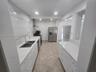 Kitchen featuring white shaker-style cabinetry, quartz countertops, full-height stone-look backsplash, stainless steel appliances, and tile flooring