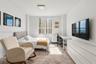 Bright interior space featuring a large window with urban and water scenery, neutral wall finishes, and a modern ceiling-mounted light fixture