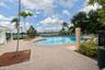 In-ground pool with paved surround, covered patio structure, and waterfront backdrop