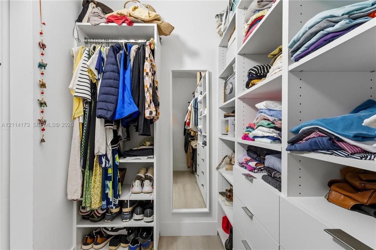 Walk-in closet featuring extensive built-in white shelving, integrated clothing rods, multiple pull-out drawers with metal hardware, and a full-length