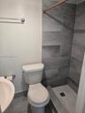 Bathroom featuring a shower stall with large-format stone-finish wall tile, a mosaic-tiled floor, a pedestal sink, and a high-profile toilet