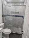 Walk-in shower featuring a sliding glass enclosure, rainfall showerhead, integrated tiled wall niche, and contrasting decorative accent tile
