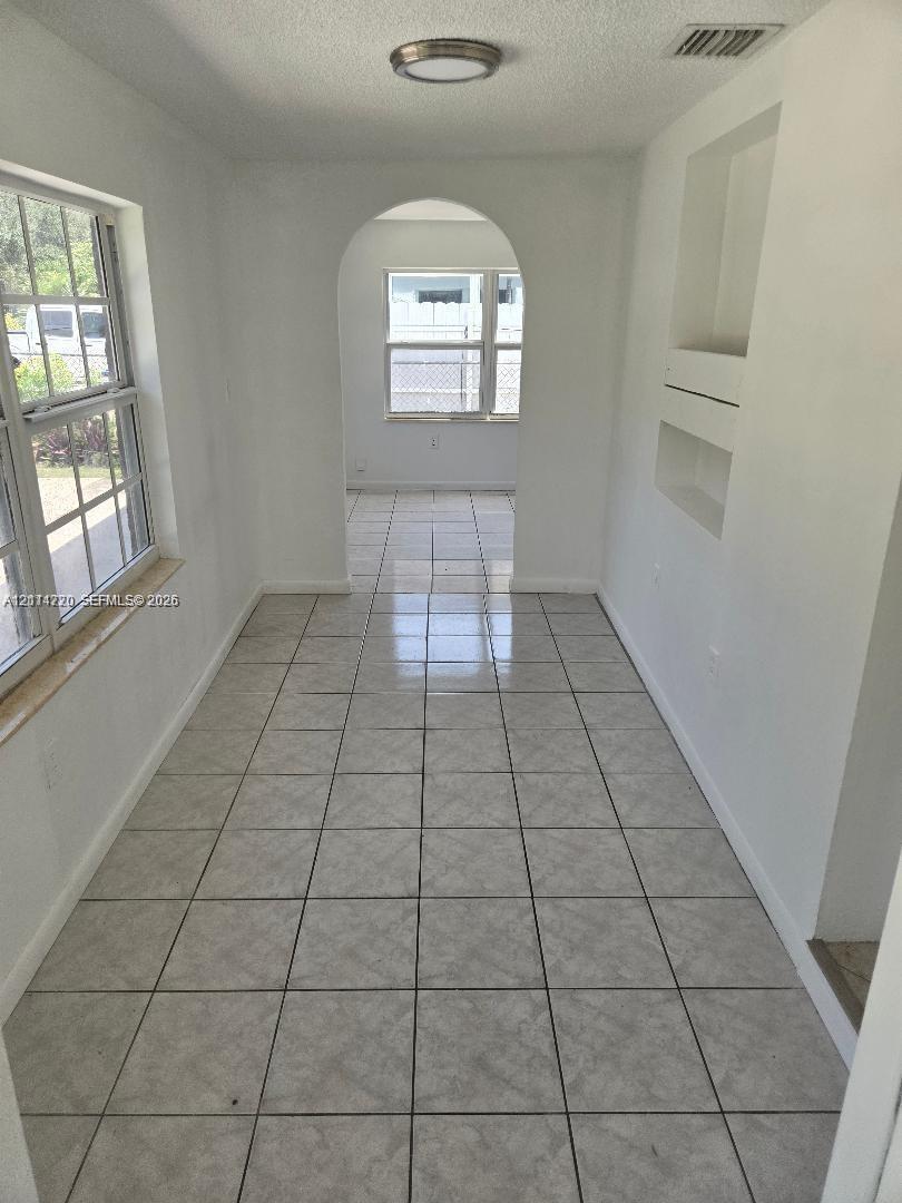 Interior space featuring tile flooring, a rounded archway, built-in wall shelving, and large windows with stone sills