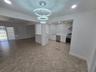 Open-concept kitchen featuring white cabinetry, stone-patterned slab backsplash, stainless steel appliances, tiered crystal chandelier, and tile floor