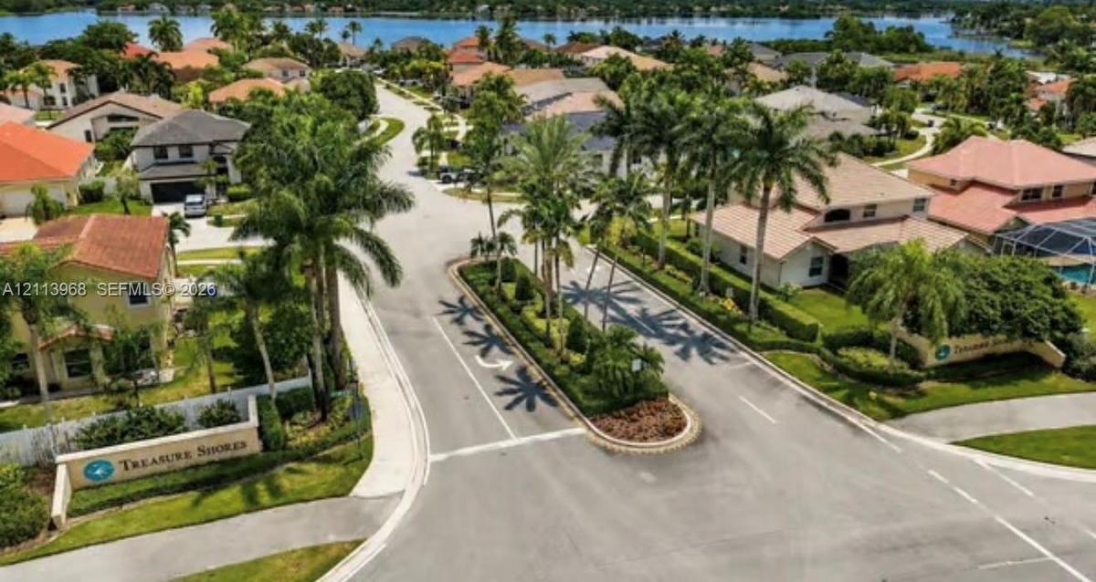 Aerial perspective of the Treasure Shores community entrance featuring a landscaped center median, palm tree-lined streets, and a waterfront position