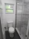 Glass-enclosed shower with horizontal wall tile, mosaic accent strip, and dark floor tiling, complemented by a single-flush toilet and a horizontal sl